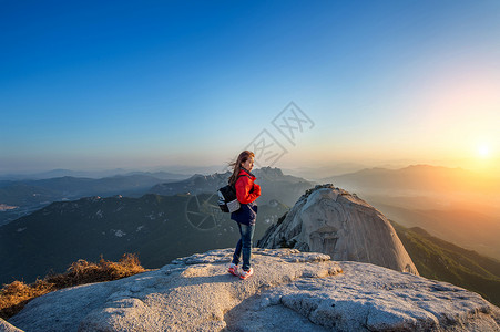 女人站在韩国首尔北汉山公园的石峰上观看日出美丽的时刻图片