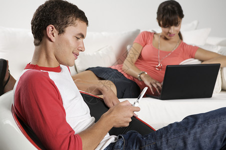 青年男子使用手机而青年妇女则坐在沙发上图片