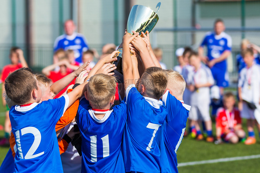 拿着奖杯的年轻足球员庆祝足球橄榄球冠军的男孩为孩子们赢得体图片