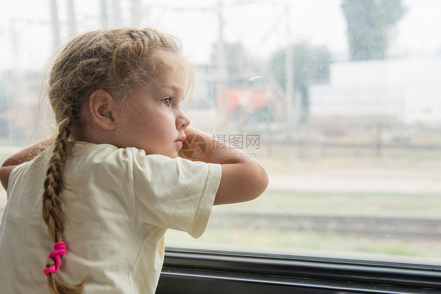 四岁女孩在二等列车中与货架底侧的窗外看望着窗户坐图片