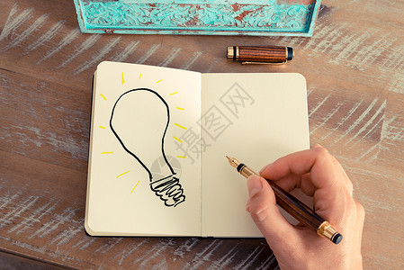 复古效果和女人手在笔记本上用钢笔画灯泡的色调图像图片