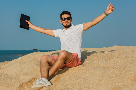 在海边的太阳镜上工作坐在沙滩上的小男孩图片