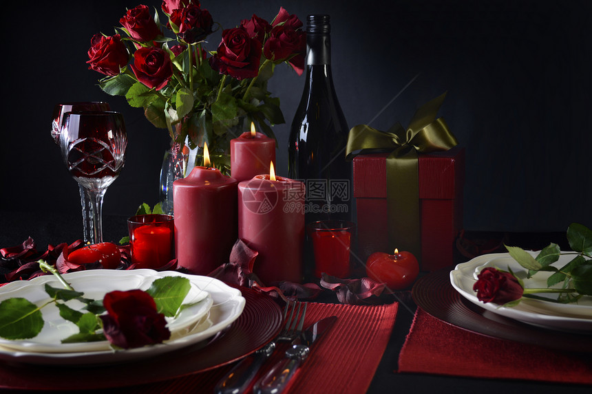 配有红玫瑰礼物和在黑色背景下烧蜡烛的两台浪漫烛光图片
