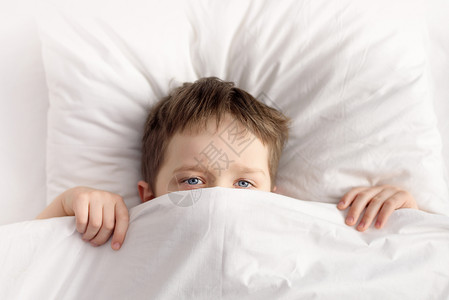 小男孩躲藏在白毯子或家庭隐蔽的床底下图片
