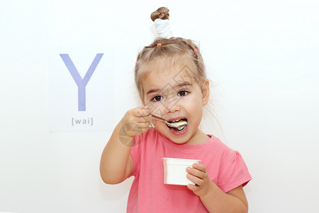 漂亮的小女孩在白色背景上吃酸奶上面写着Y字图片