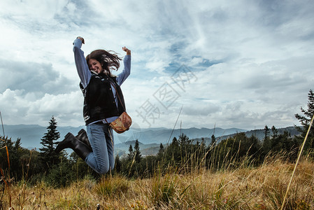 美丽的时髦旅行女孩在森林背景的山上跳到山图片