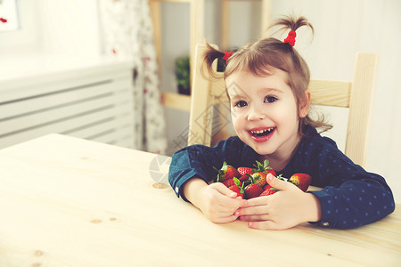 快乐的孩子女孩在夏天的家庭厨房里吃草莓图片