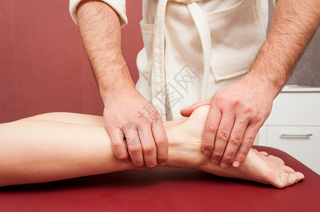 年轻妇女在温泉沙龙接受按摩师的腿按摩图片