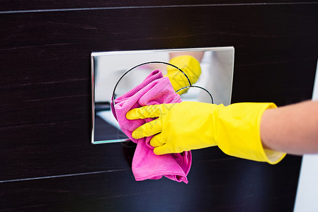 带黄色橡胶防护手套的女手用粉色布清洁马桶冲水按钮图片
