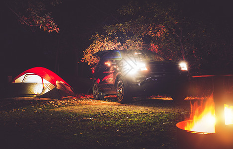 露营冒险在森林深处的帐篷露营现代越野车帐篷和野营火坑中的燃烧木图片