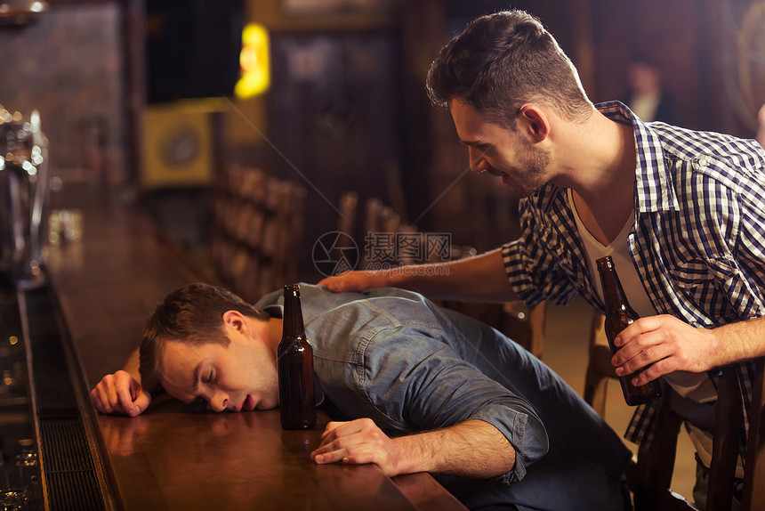 穿便衣的年轻人睡在酒厅吧柜台的啤酒瓶旁边图片