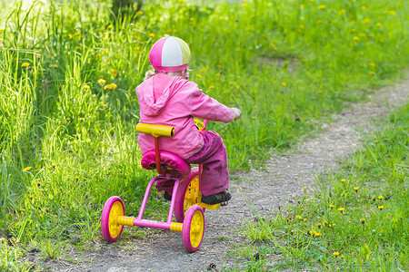 在公园赛道上带花朵的粉色和黄色三轮车场的小姑娘图片