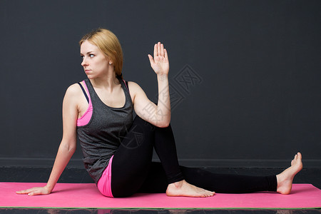 瑜伽健身体扭曲年轻女正在做对垫子和灰色背图片