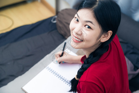 可爱的亚洲年轻女子在床上写书红衬衫图片