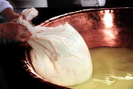 高级专家乳酪制造商从装满牛奶和油的大铜锅中用防水布收图片