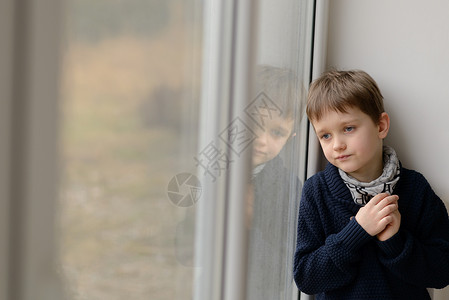 可怜的小男孩看着窗外的窗图片