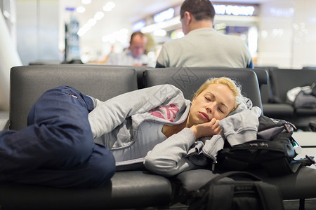 疲倦的女旅行者睡在空港出入口长凳上图片