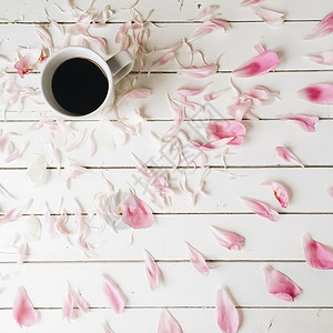 黑咖啡杯和白木背景的粉红小花图片