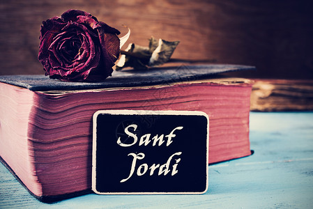 圣霍尔迪一本旧书和一朵玫瑰放在一张蓝色的桌子上背景