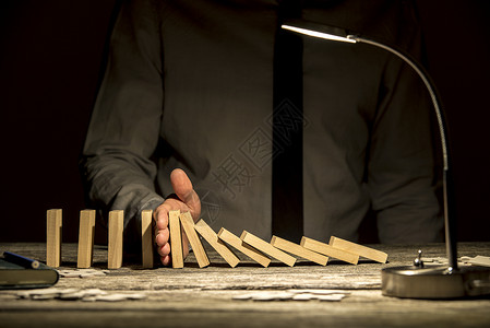 商人前视线停止掉落的多米诺人手放在木制纹纸质办公桌图片