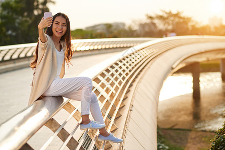 微笑的年轻女子坐在桥上自拍图片