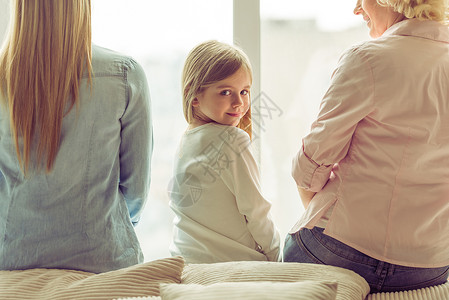 三代美女靠窗坐在沙发上的背影小女孩看着相机微笑图片