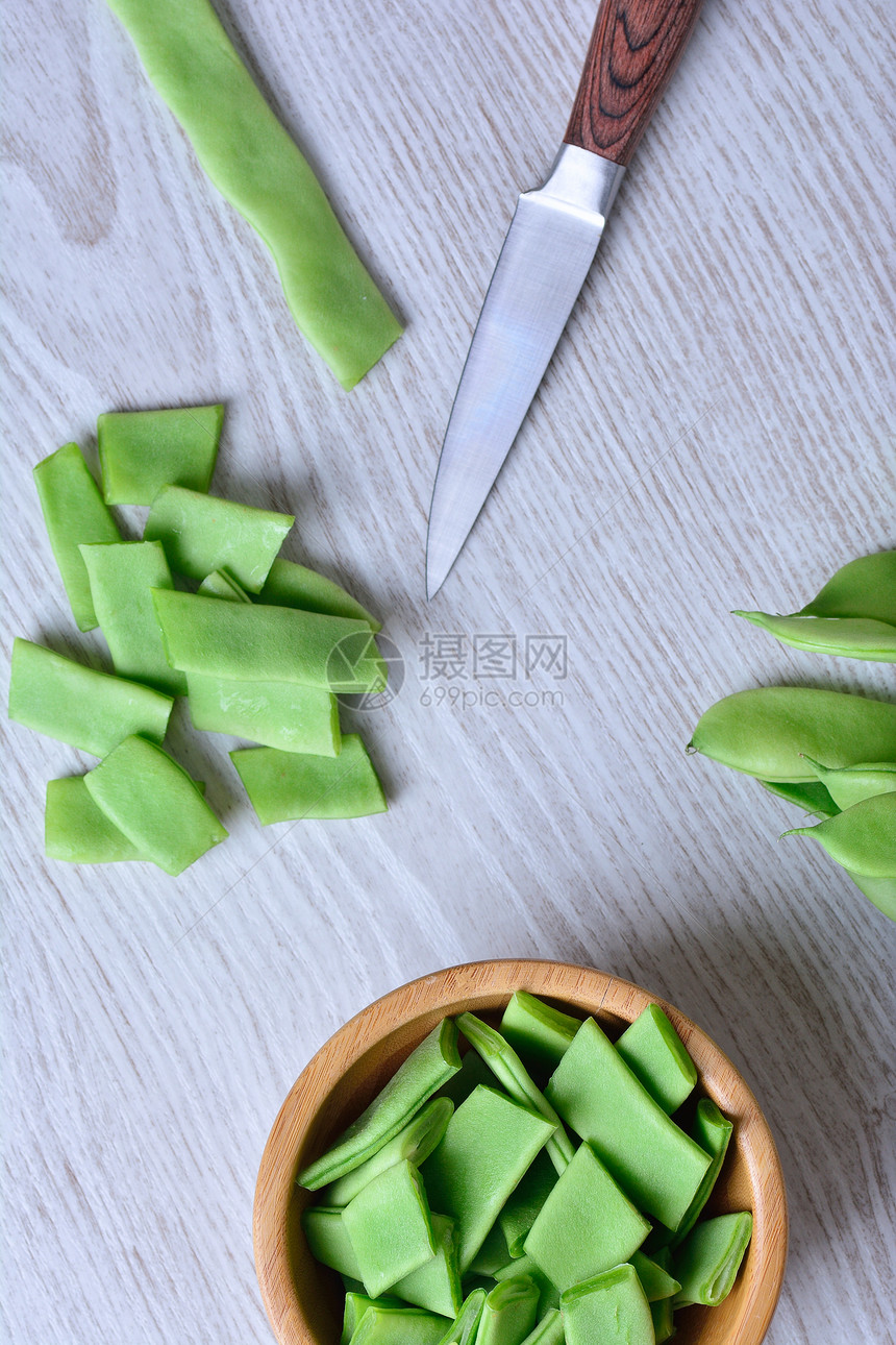 在木制桌上用刀子和碗盘切开的绿色豆图片