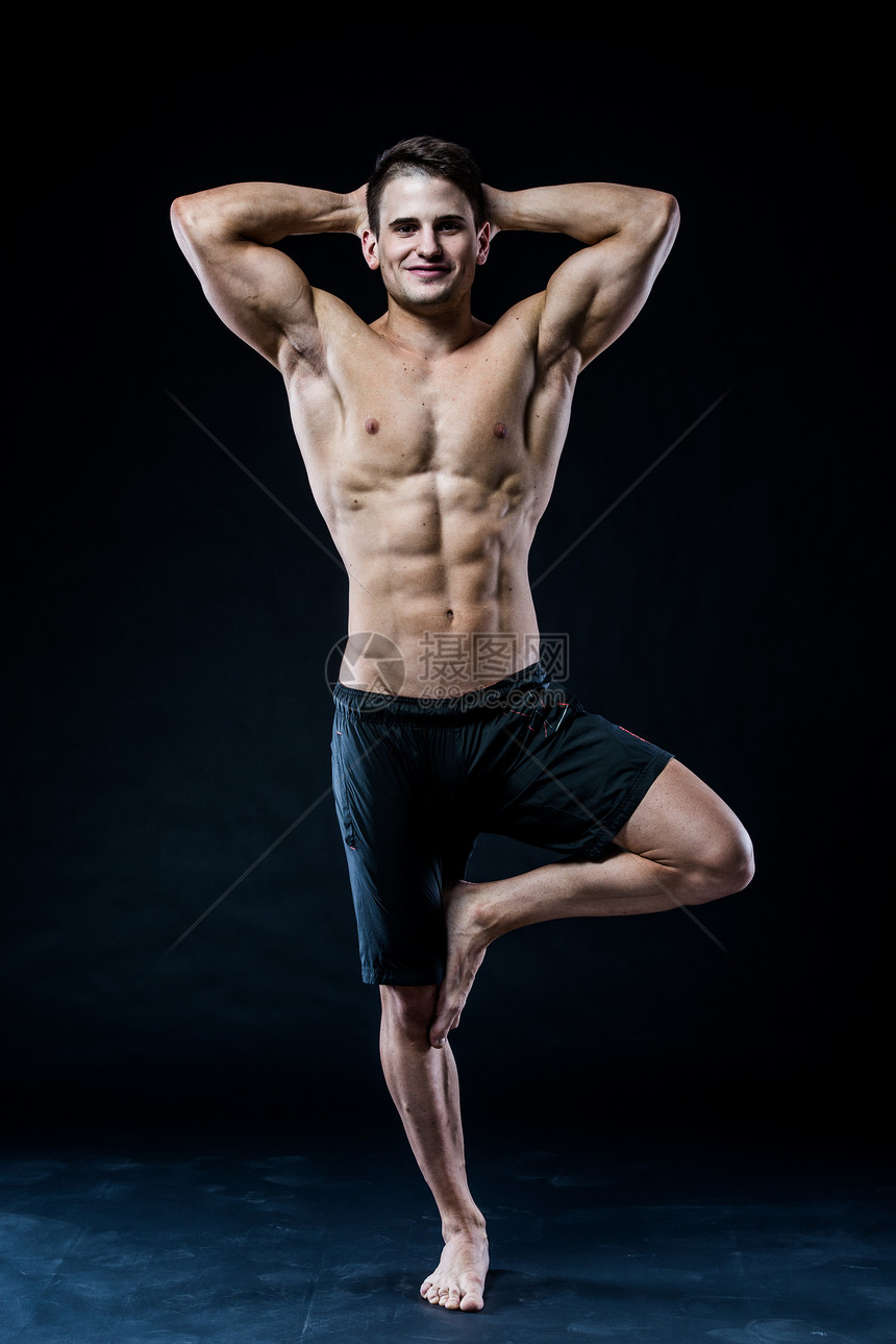 肌肉男在一腿上保持平衡在黑暗背图片