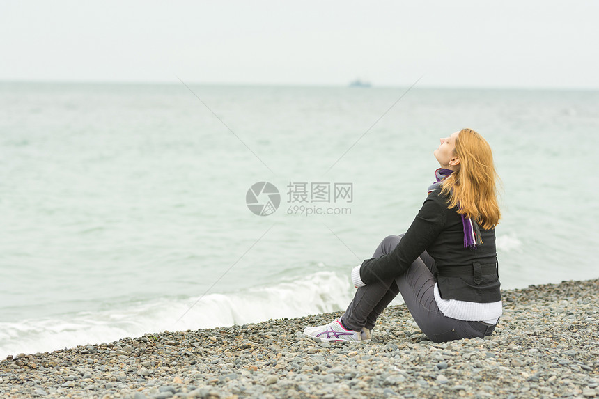 阴天小女孩坐在海边的卵石滩图片