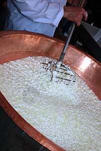 起司匠把凝乳和牛奶搅拌到大铜锅里图片