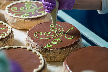 带有绿色装饰的棕色蛋糕工人手工装饰蛋糕把奶油放在蛋糕表图片
