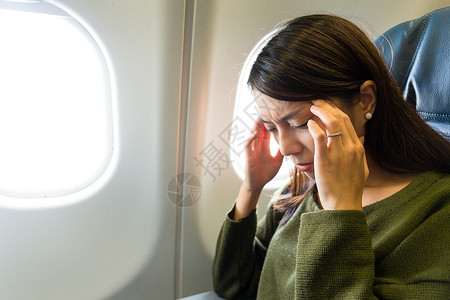 坐在飞机上的亚裔年轻女子因头痛而图片
