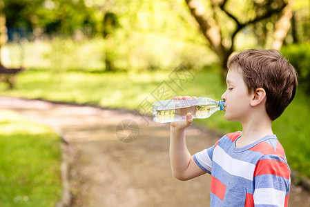 可爱的小男孩喝矿泉水从公园的塑图片
