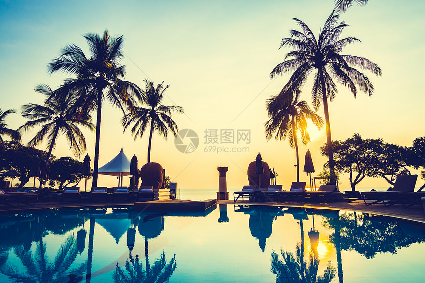 日出时酒店度假村室外游泳池周围美丽的豪华雨伞和椅子和椰子树图片