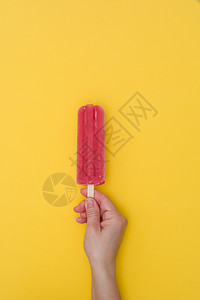 黄色背景中手持草莓冰棒的手图片