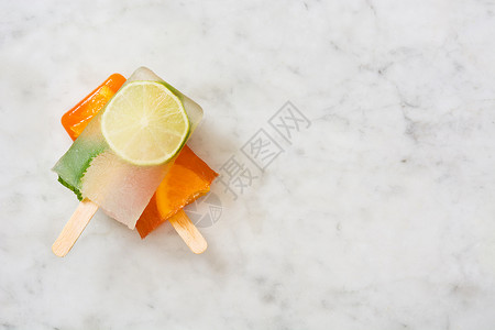 大理石桌上的橙色冰棒和石灰冰棒背景图片