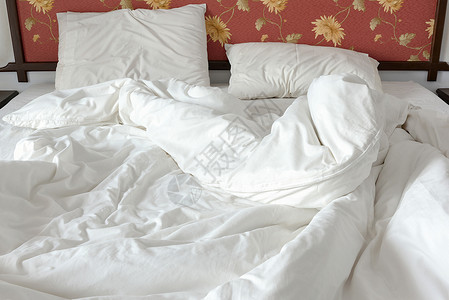 未整理不整洁的床铺有白色皱巴的毯子和两个凌乱的枕头在卧室里图片