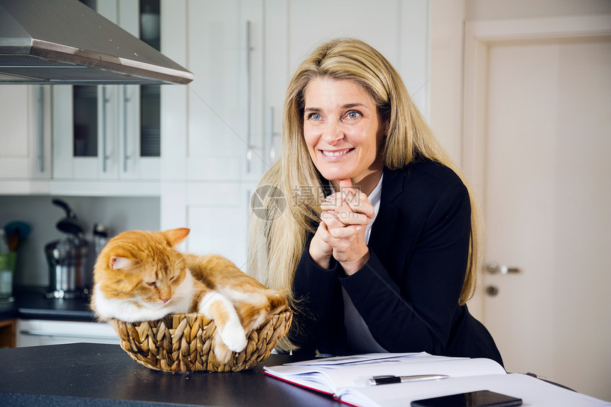 有吸引力的中年女商人在厨房里和她的猫合影红头发的猫坐在她旁边的编织篮子里在家轻图片