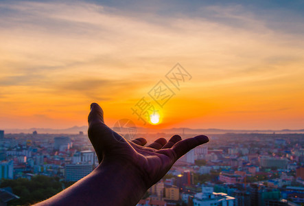 手拿着日落和城市的背景图片