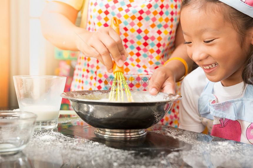 亚洲小女孩和妈喜欢在现实生活中的厨房里装饰蛋糕图片