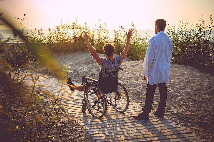 坐在轮椅上的年轻人和他的医生在日落图片