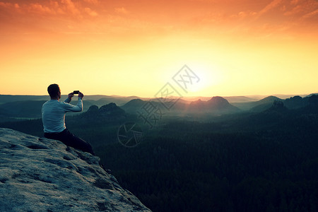 穿着灰色t恤的游客在岩石峰上用智能手机拍照下面是梦幻般的丘陵景观图片