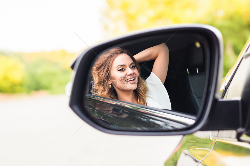 快乐的年轻女司机看着汽车侧视镜图片