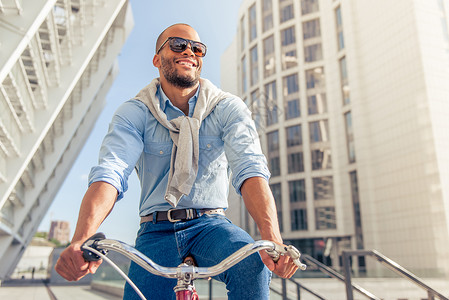 穿着便衣戴太阳眼镜的英俊年轻非裔美国人男子骑着自行车微图片