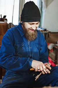 穿着蓝色牛仔裤西装和黑帽子的留胡子的男人用乐器刻木头看着木勺图片