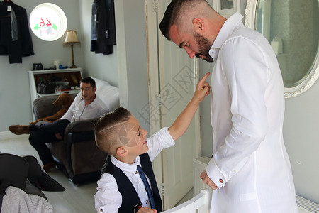 一个年轻男孩在结婚日给父亲穿衣服图片