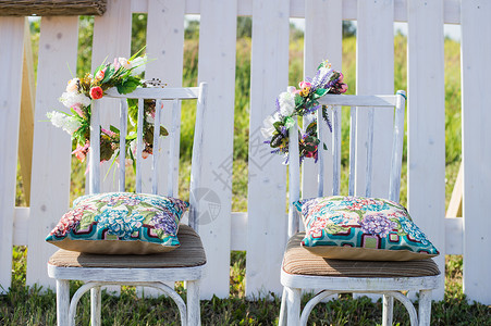 两张古老的白色椅子多彩的天鹅绒枕头和用花朵装饰的背景壁栅栏图片