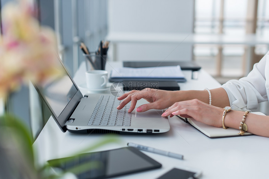 使用键盘在现代办公室用便携式计算机工作的女手和配件的近照片图片