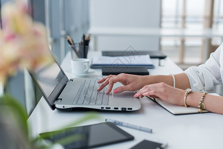 使用键盘在现代办公室用便携式计算机工作的女手和配件的近照片图片