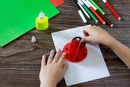 孩子将纸张细节粘在明信片上孩子用瓢虫做明信片木桌上的胶水纸剪刀儿童艺术项目背景图片